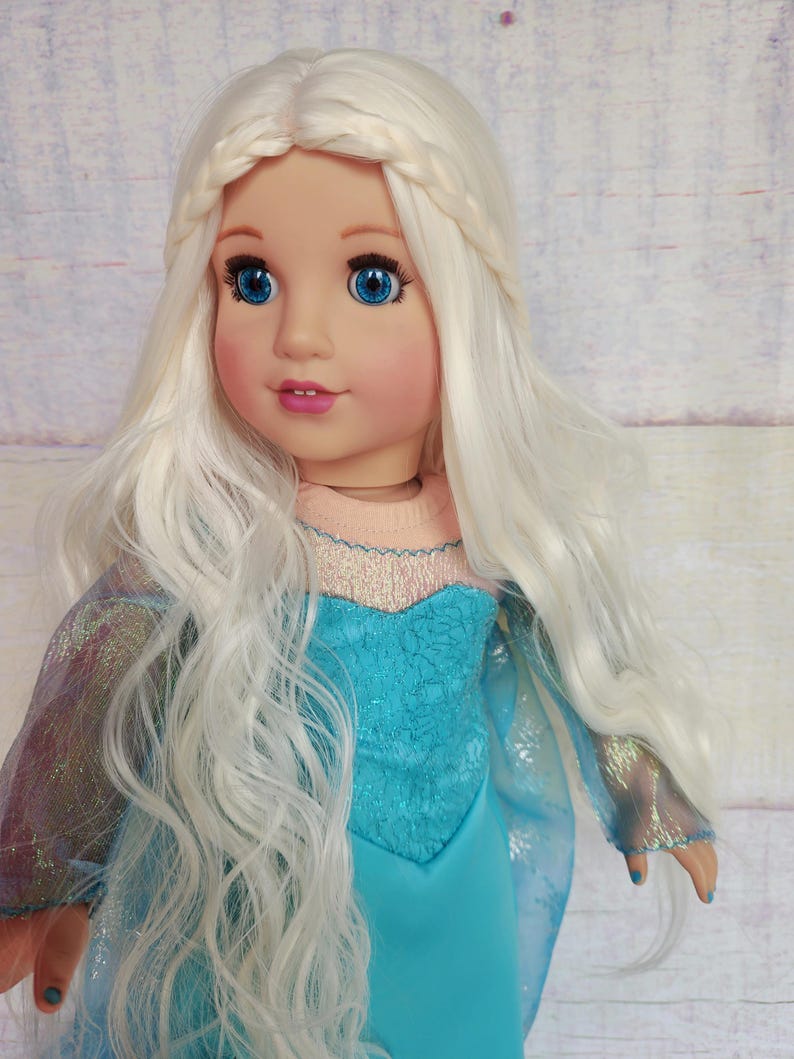 May include: A doll with long, white, wavy hair styled in a braid. The doll is wearing a blue dress with a sparkly bodice and a sheer overlay.