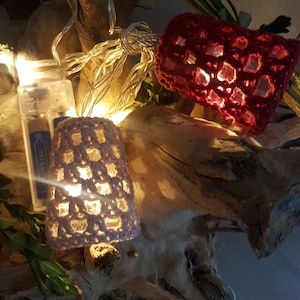 Puede incluir: Un conjunto de luces de cadena con cubiertas de ganchillo. Las cubiertas son de color rosa y blanco. Las luces están enhebradas en una rama.
