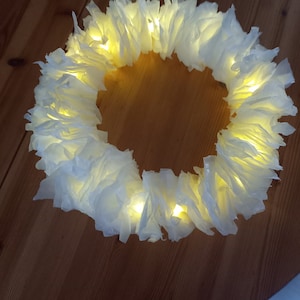 Könnte beinhalten: Ein weißer Papierkranz mit warmweißen LED-Lichtern, die um ihn herum gespannt sind. Der Kranz besteht aus vielen Papierschichten, die ein flauschiges und strukturiertes Aussehen erzeugen.