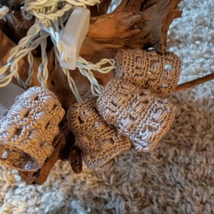 Könnte beinhalten: Ein Satz gestrickter beigefarbener Lichterabdeckungen für eine Lichterkette. Die Abdeckungen sind auf einem Stück Treibholz angeordnet.