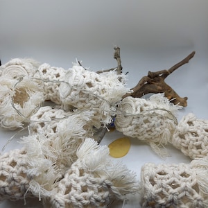 Pode incluir: Uma corda de luzes brancas de crochê com uma borda desfiada e um galho de madeira natural. As luzes são enfiadas com um fio transparente.
