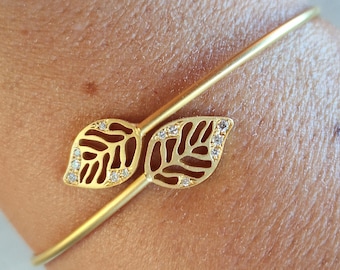 May include: Gold-toned bracelet featuring a leaf design. The leaves are adorned with small, sparkling embellishments. The bracelet is a delicate piece of jewelry, perfect for adding a touch of elegance to any outfit.