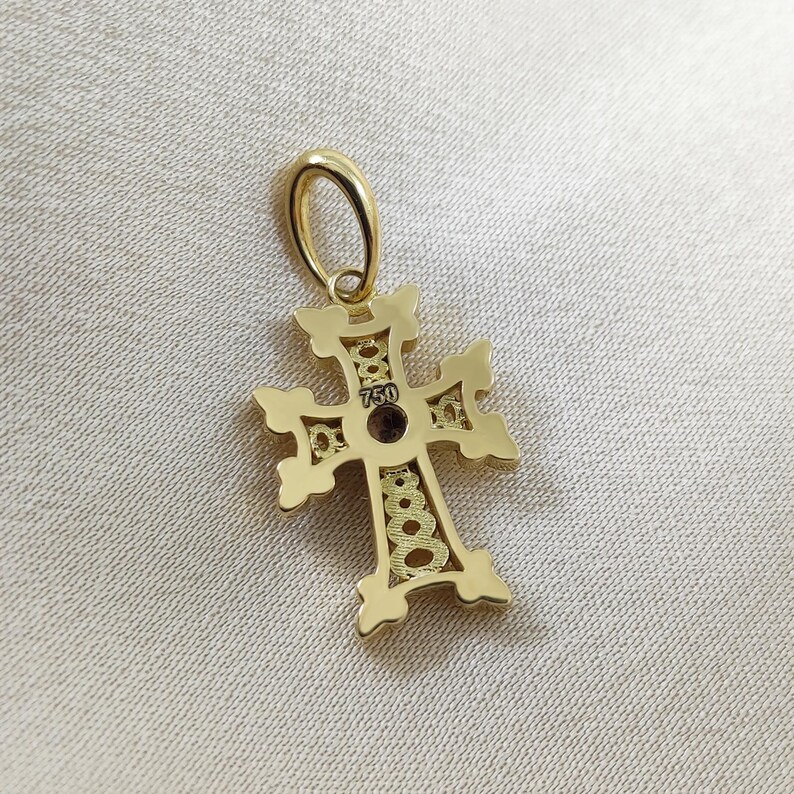 May include: Gold cross pendant with intricate detailing. The back of the pendant has the number "750" stamped on it.