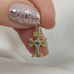 May include: A gold cross pendant with a clear gemstone in the centre. The cross has intricate details and a delicate design.