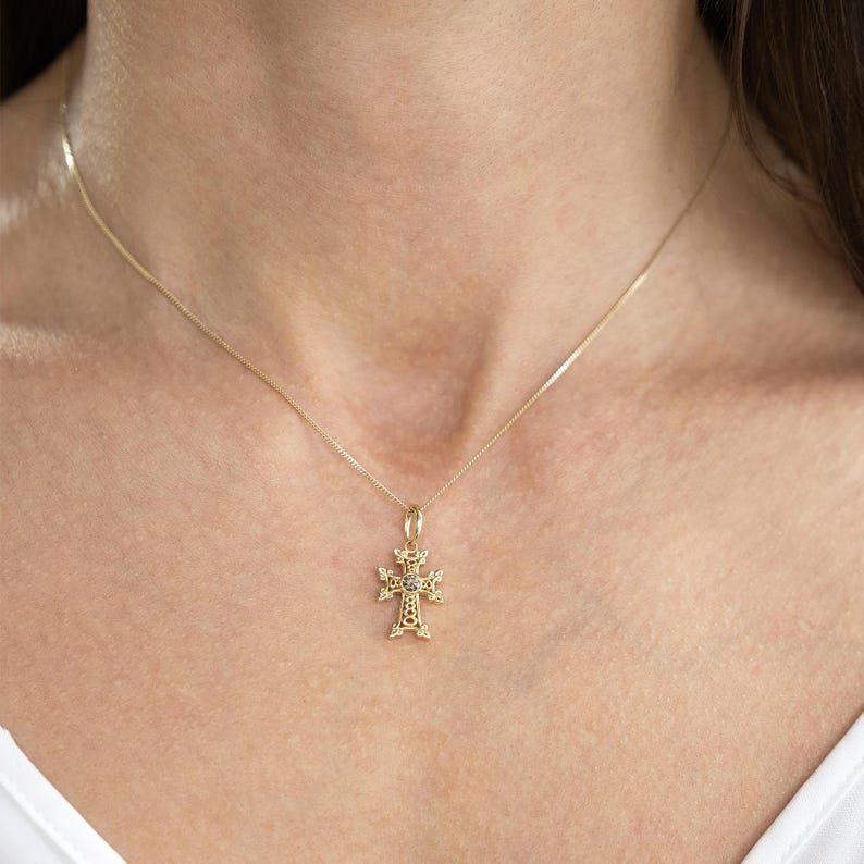 May include: A gold chain necklace with a delicate, ornate cross pendant featuring a small, clear gemstone in the centre.