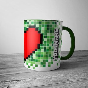 Può includere: Una tazza in ceramica verde e bianca con un cuore a pixel e il testo "YOUR NAME" sul lato.