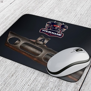 Könnte beinhalten: Eine schwarze Mausmatte mit einem braunen Metallobjekt und einer Grafik von drei maskierten Figuren mit dem Text "YOUR NAME" in Rot und Weiß.