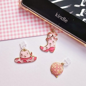 May include: Three pink and gold charms: a cowboy hat, a cowboy boot, and a disco ball. The cowboy hat has a pink polka dot pattern and star accents. The cowboy boot has star accents. The disco ball has a checkered pattern.