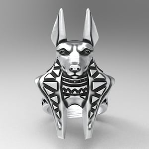 K&ouml;nnte beinhalten: Ein silberner Ring mit einem detaillierten Anubis-Kopf und einem geometrischen Muster um den Hals. Der Ring ist ein Statement-Piece mit einem einzigartigen Design.