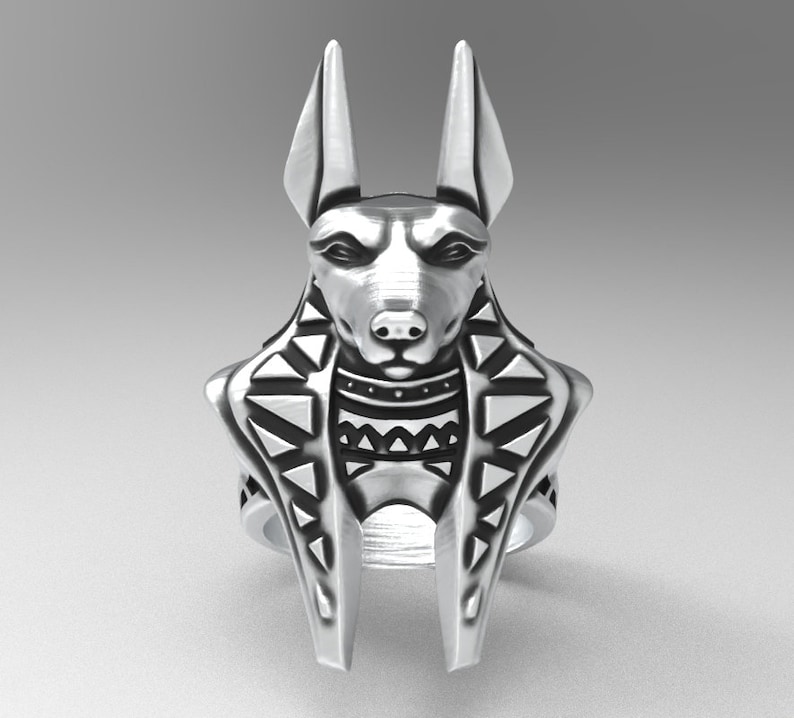 K&ouml;nnte beinhalten: Ein silberner Ring mit einem detaillierten Anubis-Kopf und einem geometrischen Muster um den Hals. Der Ring ist ein Statement-Piece mit einem einzigartigen Design.