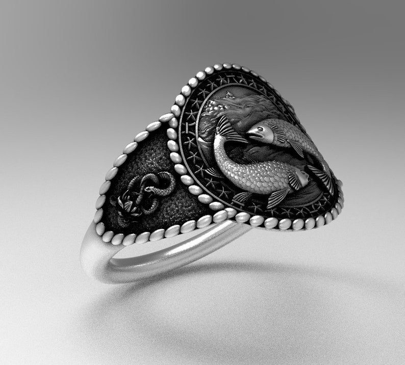 May include: A silver ring with a detailed design featuring two fish intertwined. The ring has a textured band and a decorative border.