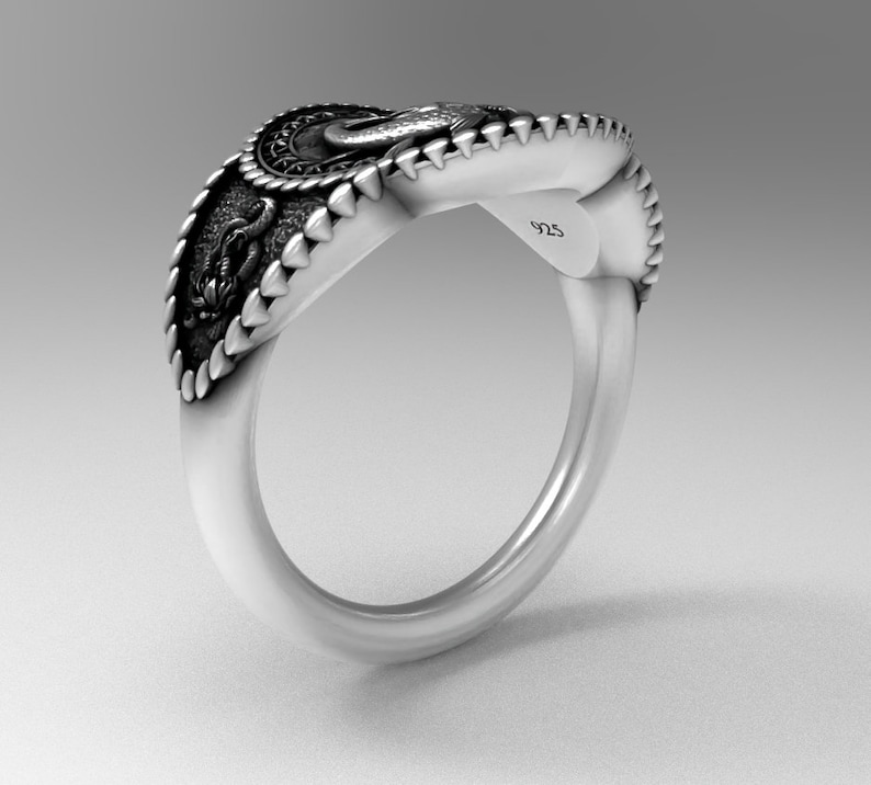 May include: A silver ring with a detailed design featuring a dragon and a crown. The ring is marked with "925" on the side.