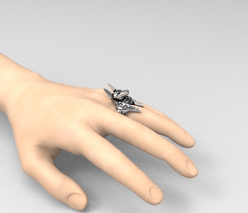 K&ouml;nnte beinhalten: Ein silberner Ring mit einem detaillierten Anubis-Kopfdesign. Der Ring wird an einem Finger getragen.