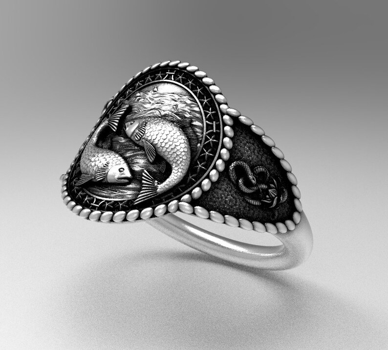 May include: A silver ring with a detailed design of two fish swimming in a circle. The ring has a rope-like border and a textured surface.