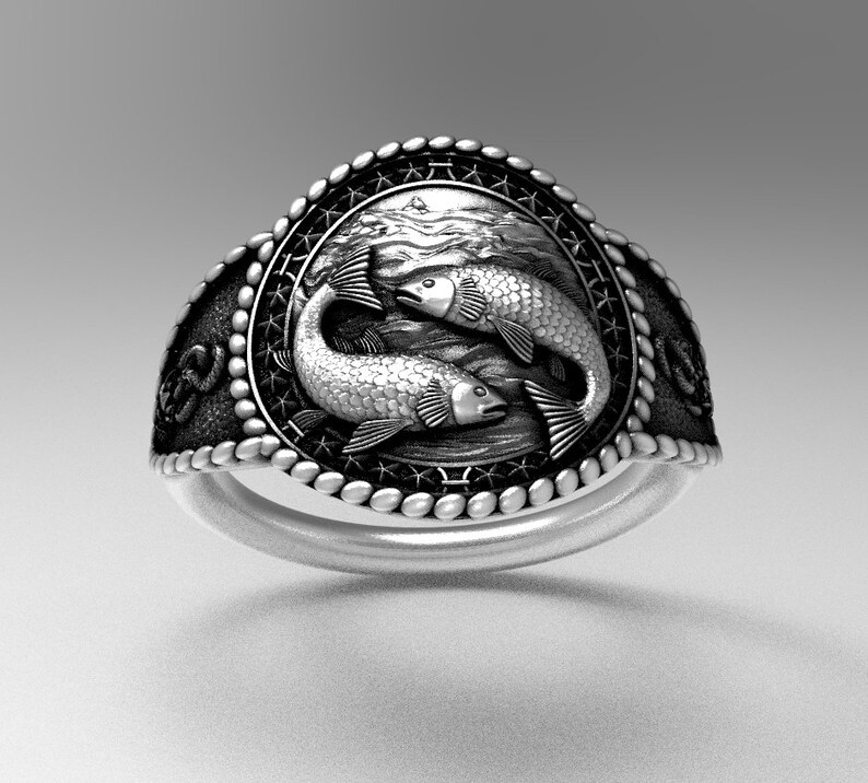 May include: A silver ring with a detailed design of two fish swimming in a circle. The ring has a textured band and a black background.
