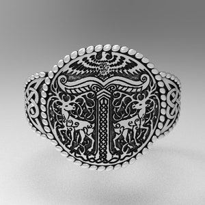 May include: A silver ring featuring a detailed design of a stylised tree, two deer and an eagle. The ring is decorated with a Celtic knot pattern.