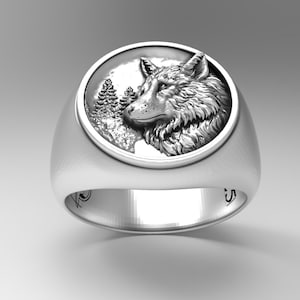 May include: A silver ring with a detailed wolf head design in a circular frame. The wolf is shown in profile, set against stylized trees and a cloudy sky. The ring has a polished finish and a wide band. The ring is made of silver.