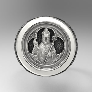 Op de afbeelding: Een zilveren ring met een gedetailleerd ontwerp van een religieuze figuur in een bisschopsmitra en gewaden, die een staf vasthoudt. De figuur wordt omringd door een decoratief bloemmotief.