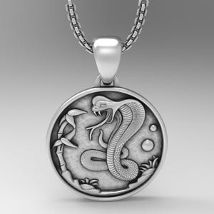May include: Silver pendant necklace featuring a detailed cobra snake design with a raised head and a bamboo stalk in the background. The pendant is round and has a smooth, polished finish.