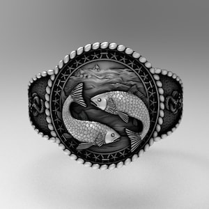 May include: A silver ring with a detailed design of two fish swimming in a wave pattern. The ring is surrounded by a rope-like border with stars.
