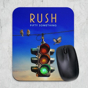 Può includere: Un tappetino per mouse rettangolare con sfondo cielo blu e il testo RUSH FIFTY SOMETHING in giallo. Un semaforo pende da un filo con due uccelli appollaiati e uno in volo. Un mouse per computer nero è appoggiato sul tappetino.