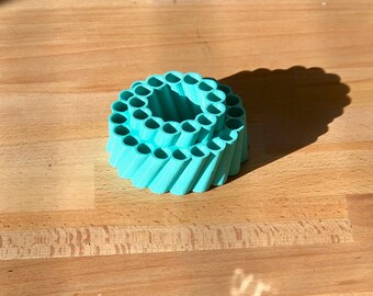 Op de afbeelding: Een turquoise blauwe plastic potloodhouder met een spiraalvormig ontwerp. De houder heeft meerdere vakken voor potloden of andere schrijfbenodigdheden.