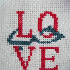 May include: A close-up of a white fabric with red and blue embroidery spelling out the word "LOVE".