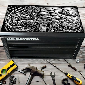 May include: Black US General tool chest with a black and white graphic of a soldier and American flag on the lid. Tools, including a spirit level, hammer, and spanner, surround the chest.