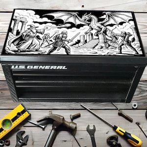 Puede incluir: Caja de herramientas negra U.S. General con una escena de arte fantástico en blanco y negro en la tapa. La obra de arte representa un mago, guerreros, un dragón y un arquero. Varias herramientas, incluyendo un nivel, un martillo y una llave inglesa, están esparcidas alrededor de la caja.