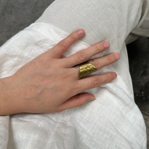 Puede incluir: Un anillo de color dorado con un diseño texturizado en forma de hoja. El anillo se lleva en el dedo índice de una mano.