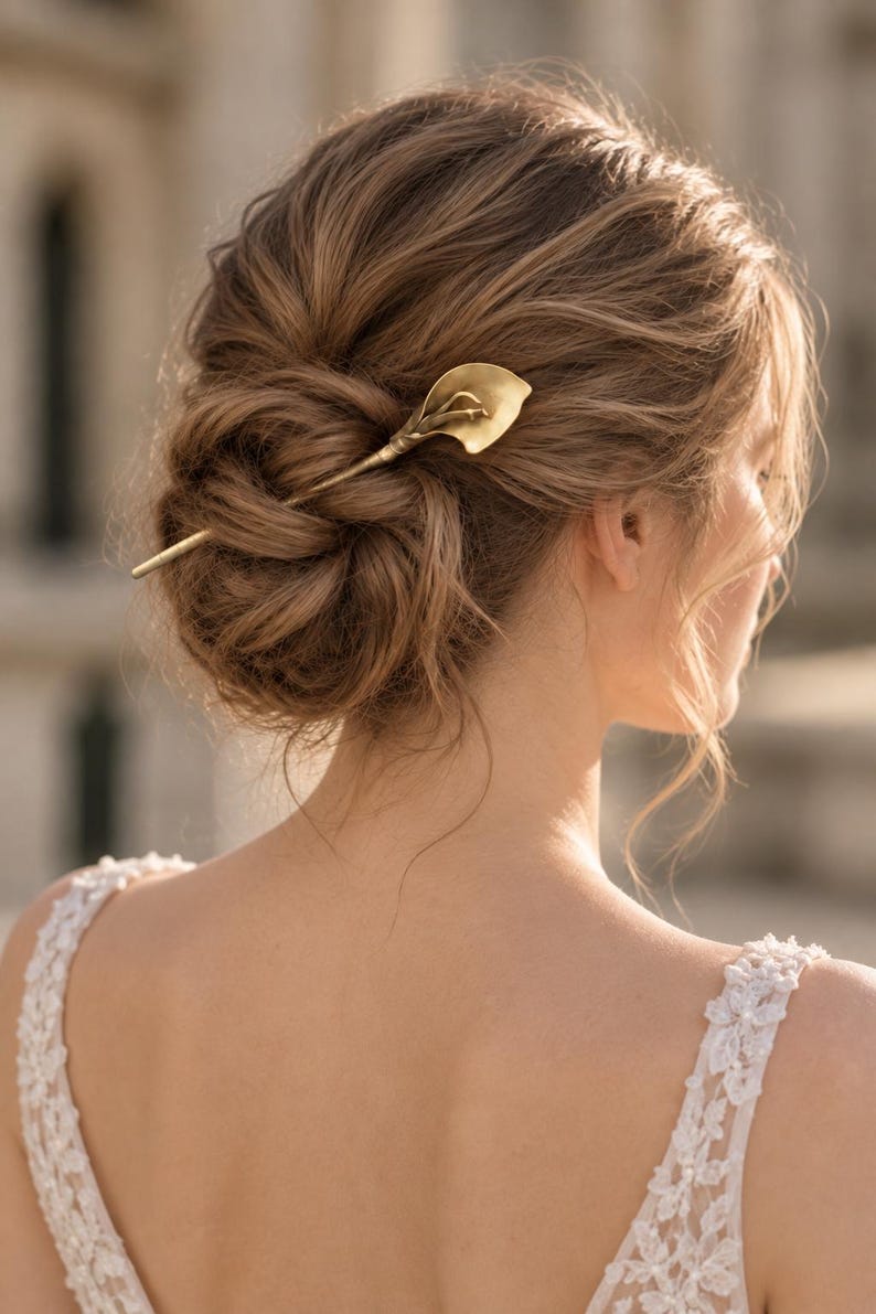 May include: A gold-toned metal hair pin shaped like a calla lily flower. The pin features a long, slender stem that secures into a styled updo, with the curved, trumpet-shaped petal of the lily resting against the hair to serve as a decorative accent.
