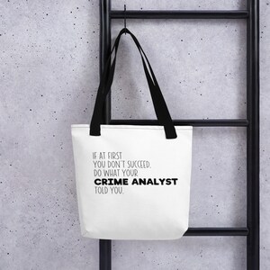 May include: White tote bag with black handles and the text "IF AT FIRST YOU DON'T SUCCEED. DO WHAT YOUR CRIME ANALYST TOLD YOU."