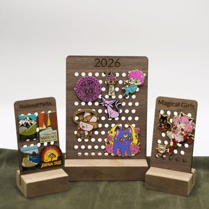 May include: Three wooden pegboard displays for enamel pins. The left board is labeled National Parks, the center board is labeled 2026, and the right board is labeled Magical Girls. Each board features rows of holes for organizing various pins.