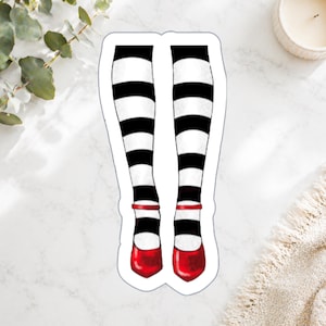 May include: A sticker featuring a whimsical illustration of legs wearing black and white striped stockings and red shoes. The shoes have a strap around the ankle. The sticker is on a white background.