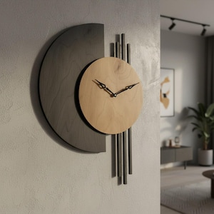 Puede incluir: Un reloj de pared moderno con un diseño único. El reloj presenta una esfera circular de madera clara con manecillas negras, sobre un fondo semicircular gris oscuro. Barras verticales negras cuelgan debajo de la esfera, agregando un toque contemporáneo. El reloj está montado en una pared gris texturizada.