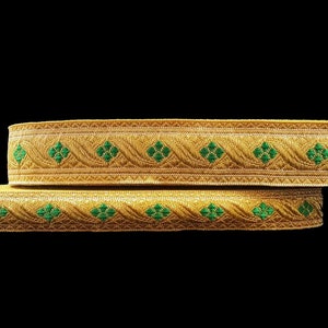 May include: Two gold-colored decorative ribbons with a repeating pattern of green floral designs. The ribbons are stacked on top of each other against a black background. The ribbons are likely used for embellishments.