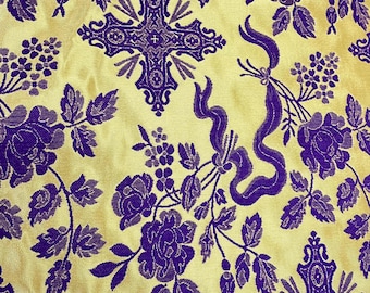 May include: Close-up of a fabric with a repeating pattern of purple floral designs, crosses, and ribbons on a yellow background. The fabric has a satin-like sheen, and the details are finely woven.
