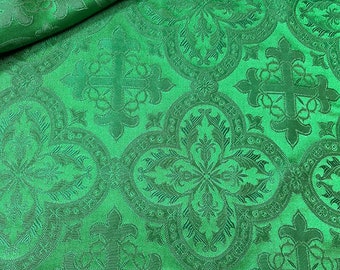Pode incluir: Tecido verde com um padrão repetitivo de cruces ornamentadas e desenhos florais. O tecido tem uma textura em relevo e um acabamento ligeiramente brilhante.