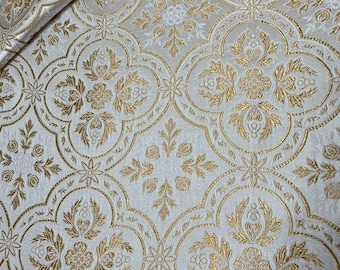 May include: White fabric with a gold brocade pattern. The pattern features a repeating design of stylized flowers and leaves.