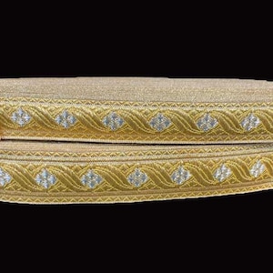 May include: Two rolls of gold ribbon with a decorative pattern. The ribbon features a repeating design of silver diamond shapes within a gold wavy border. The ribbon is likely used for crafts, sewing, or embellishments.