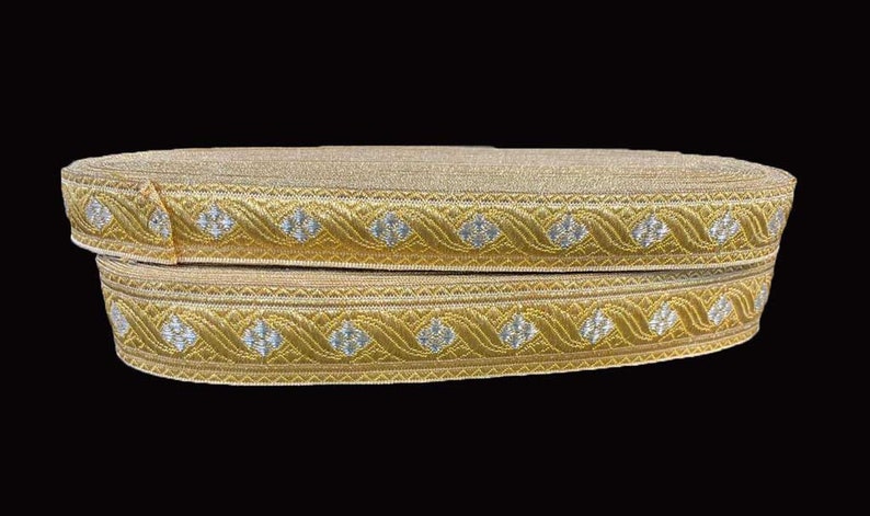 May include: Two rolls of gold ribbon with a decorative pattern. The ribbon features a repeating design of silver diamond shapes within a gold wavy border. The ribbon is likely used for crafts, sewing, or embellishments.