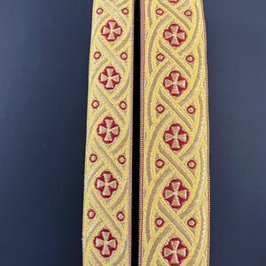 Könnte beinhalten: Zwei Stoffbänder mit einem Kreuzmuster in Gold und rotem Besatz.