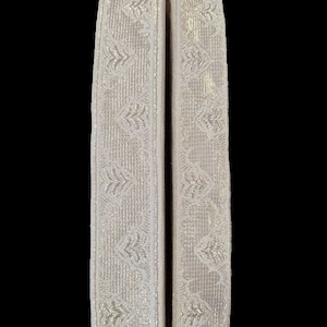 May include: Two pieces of white trim with a silver metallic pattern. The trim has a woven texture.