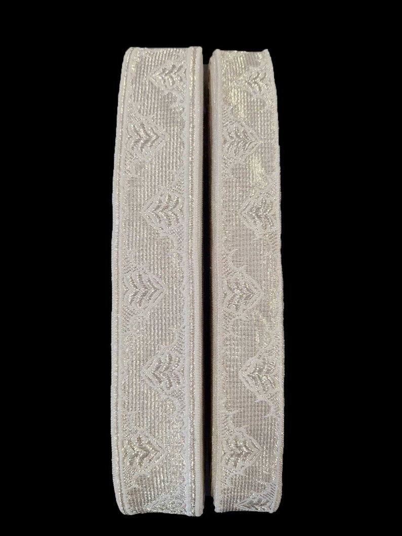 May include: Two pieces of white trim with a silver metallic pattern. The trim has a woven texture.