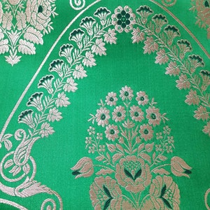 Peut inclure: Tissu vert avec un motif floral argenté. Le motif présente un grand bouquet de fleurs dans un vase, entouré de motifs floraux plus petits.