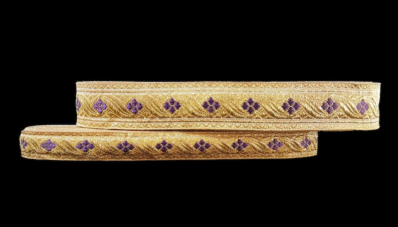 May include: Two gold-colored decorative ribbons with a repeating pattern of purple floral designs. The ribbons are layered on top of each other against a black background. The ribbons have a textured appearance.