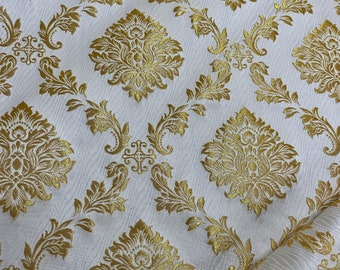 Pode incluir: Tecido branco com um padrão de damasco dourado. O design apresenta motivos florais e de rolagem repetidos em uma cor dourada metálica. O tecido tem um fundo sutil e texturizado.