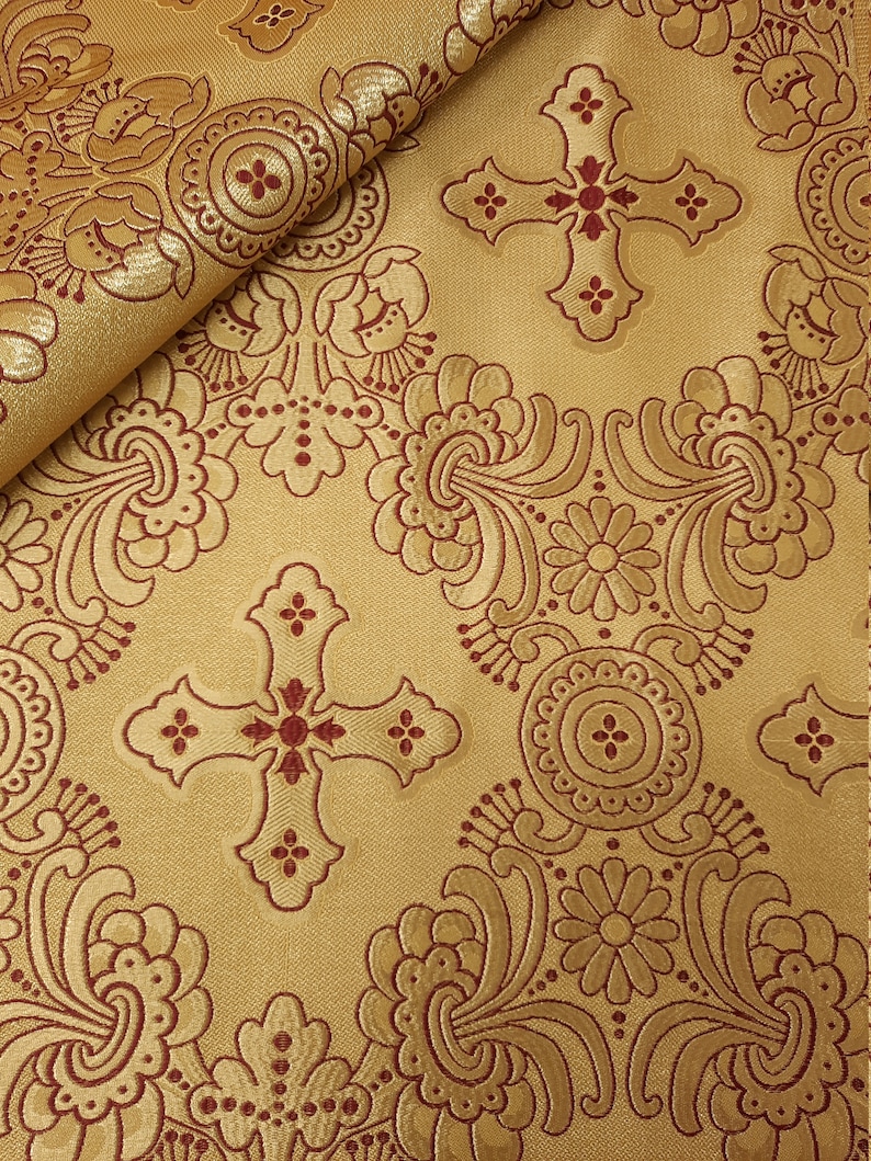 May include: Gold fabric with a red cross and floral pattern. The fabric has a raised texture.