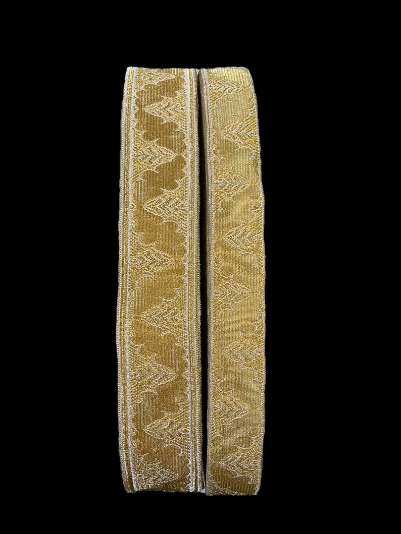 May include: Two gold-colored fabric trims with a repeating pattern of stylized leaves. The trims are approximately 1 inch wide and have a subtle sheen.