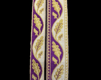 May include: Two rolls of decorative trim with a repeating pattern of gold leaves and vines on a purple background. The trim has a white border with a gold and purple zigzag edge. The trim is likely used for sewing or crafting projects.